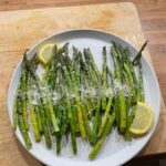 Grilled asparagus with lemon slices and Parmesan on a white plate, perfect for a healthy meal.