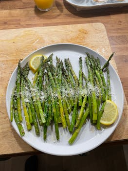 Grilled asparagus with lemon slices and Parmesan on a white plate, perfect for a healthy meal.